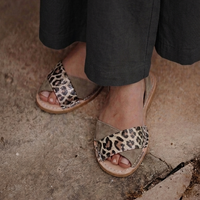A close-up of a person wearing leopard-print slide sandals with black wide-leg pants, standing on a rustic stone tile floor.