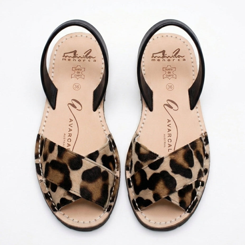 Pair of leopard print crossover avarca sandals with black straps on a white background